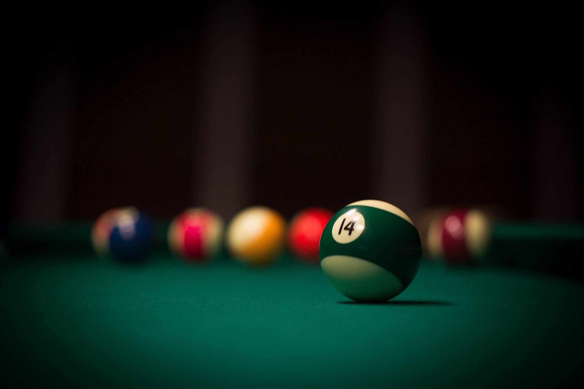Green billiard ball numbered 14 with other pool balls blurred in the background
